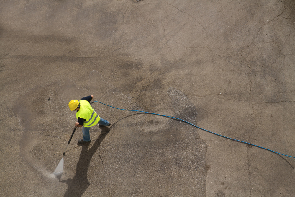 A worker pressure washing a paved jobsite area